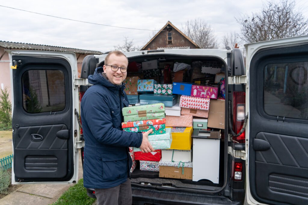 Ein Teammitglied lädt Weihnachtsgeschenke für Kinder aus dem vollen Transporter aus